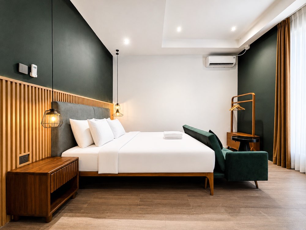 Bedroom with a king bed against a dark green wall and a green sofa