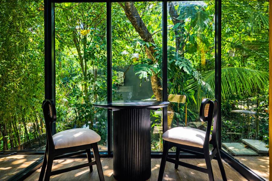 Glass corner with two chairs and a table facing the trees