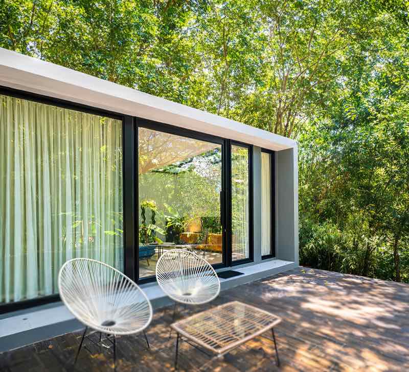 Two white wire chairs and a glass table on a forest villa deck