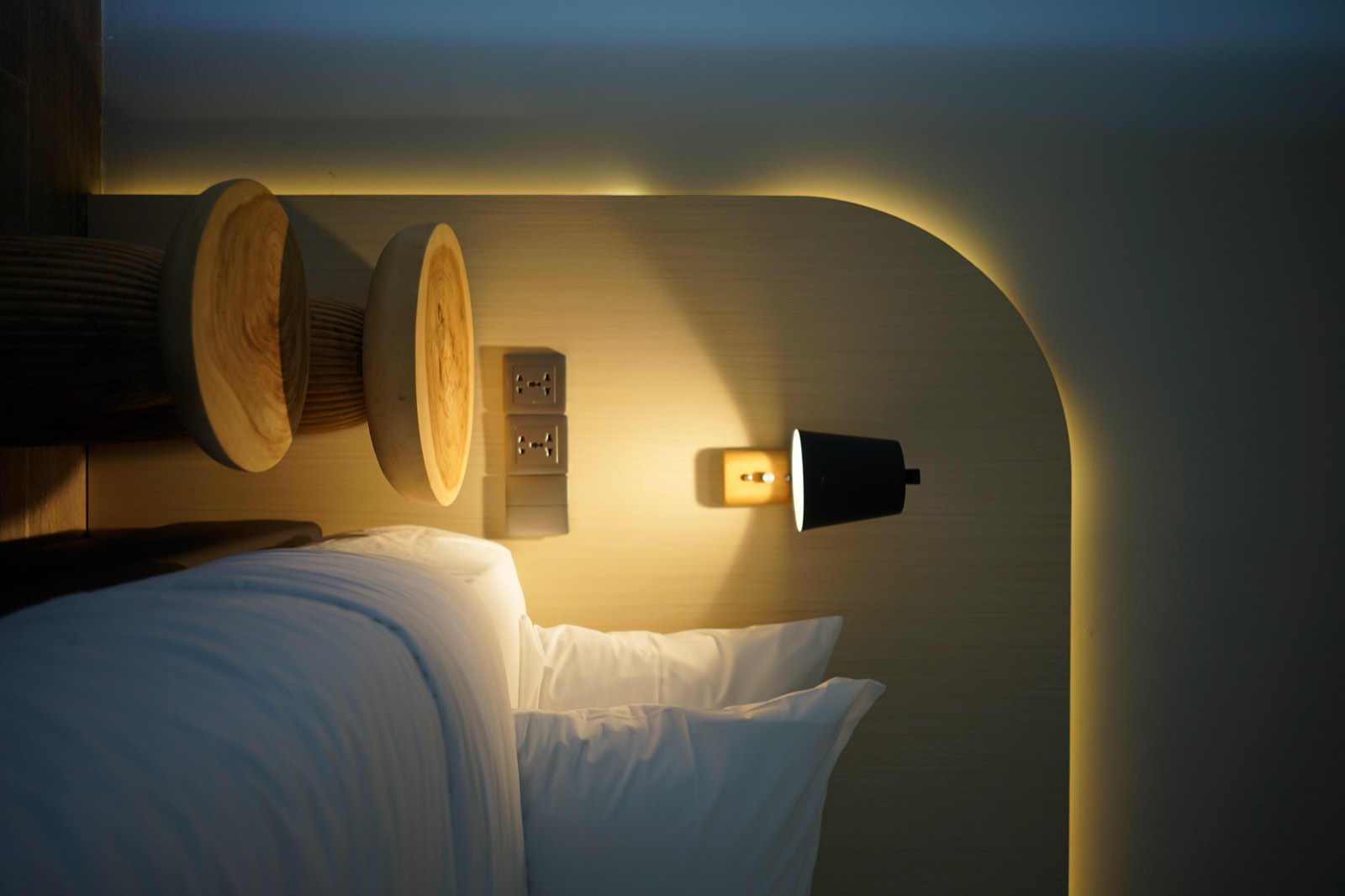 A wall lamp glowing in the arched niche beside a made bed in a forest villa