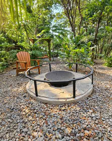 Round firepit on gravel with a wooden chair beside it