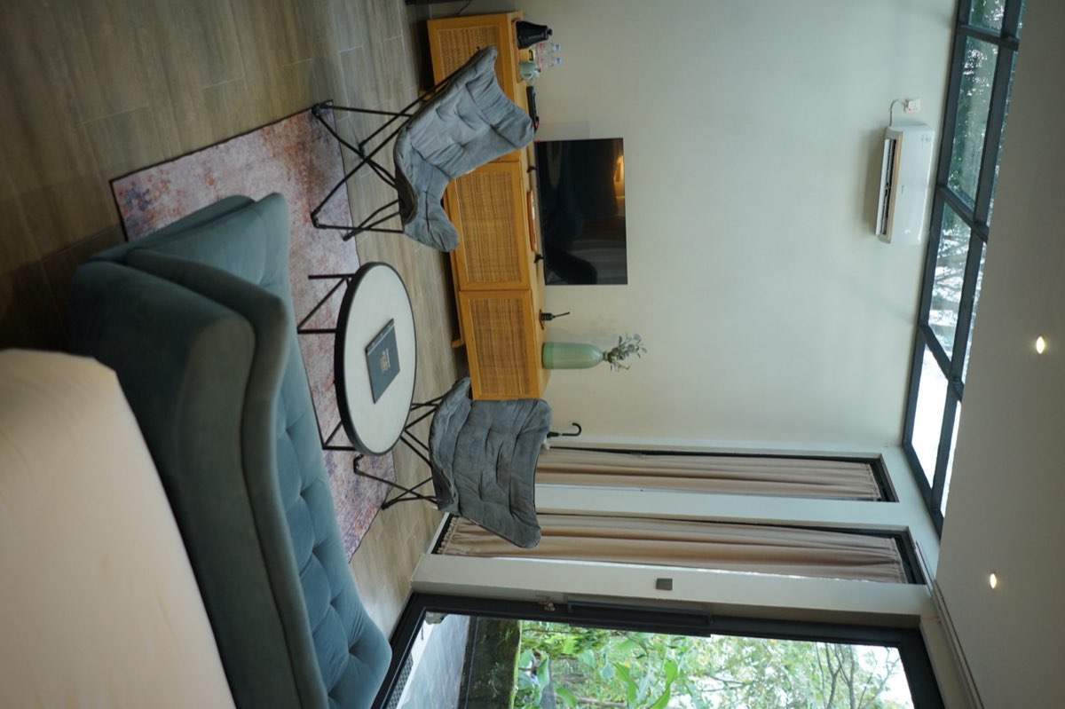 Forest Villa room with a bed, a blue sofa and two butterfly chairs by a window onto the trees
