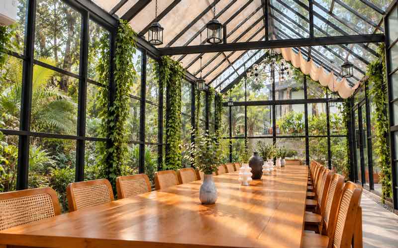 A long wooden table with rattan chairs inside the Glasshouse