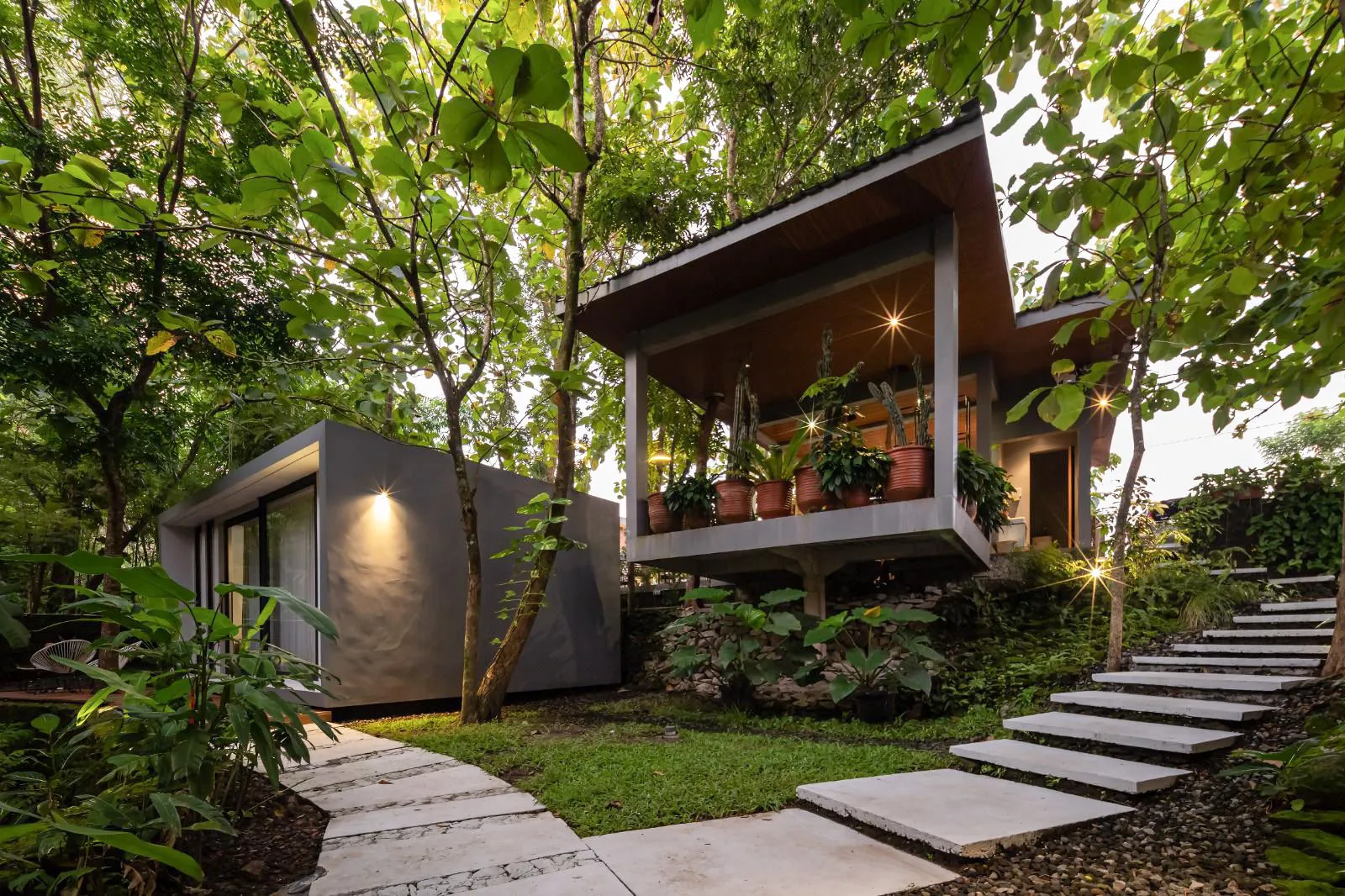 A two-storey forest villa with lit windows among tall trees, reached by stepping stones