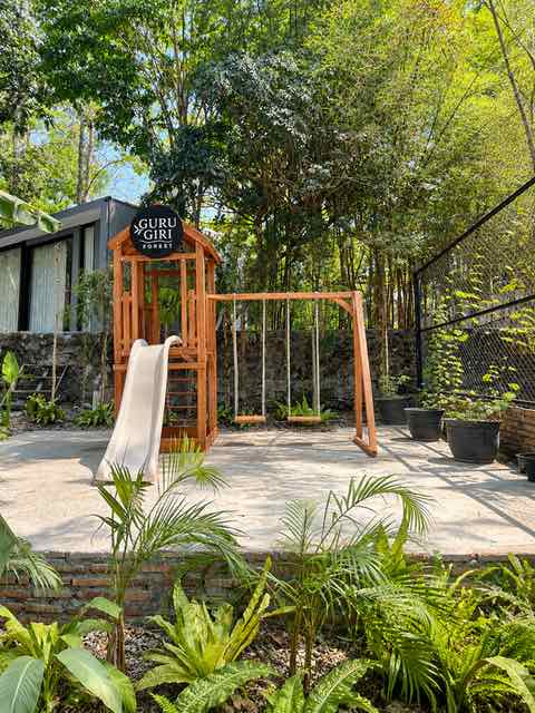 Wooden play tower with a slide and swings among palms