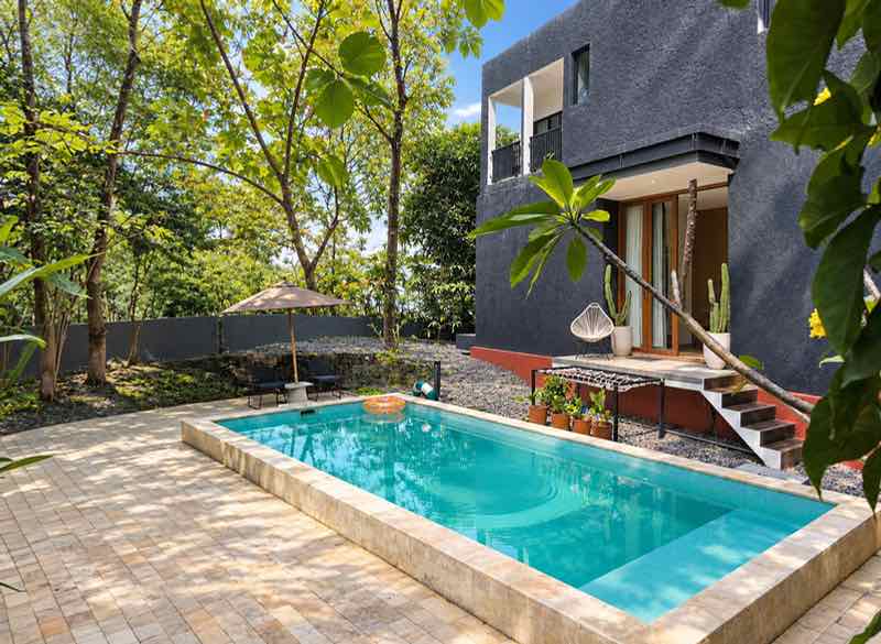 The shared pool beside a dark two-storey villa with trees around it